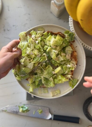 Caesar salad ground chicken pizza cut into four servings on white plate.