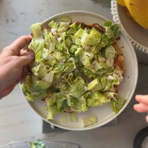 Caesar salad ground chicken pizza cut into four servings on white plate.