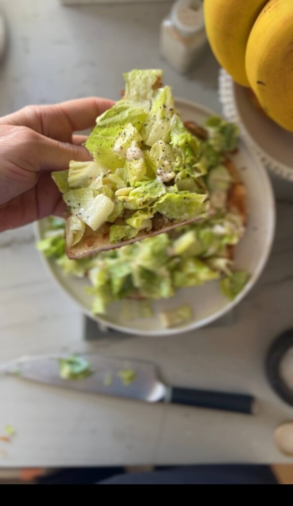 Slice of caesar salad ground chicken pizza held in hand up close.