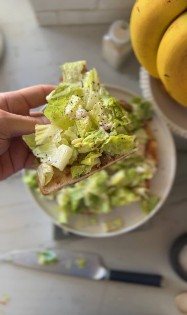 Slice of caesar salad ground chicken pizza held in hand up close.