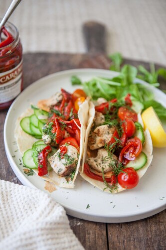 Two harissa chicken feta wraps on white plate garnished with greens and lemon wedge.