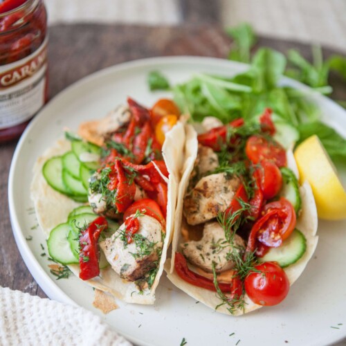 Two harissa chicken feta wraps on white plate garnished with greens and lemon wedge.