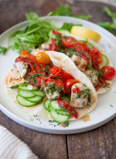 Two harissa feta chicken wraps on white plate on wood cutting board.