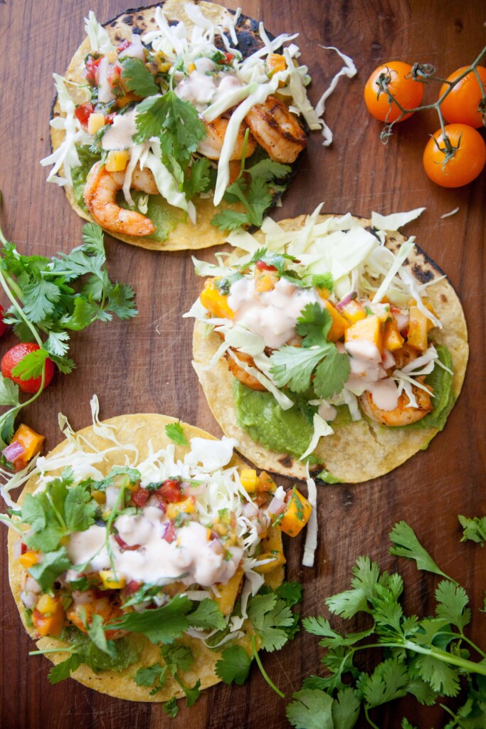 Three shrimp tacos topped with cilantro and chipotle garlic sauce on wood board.