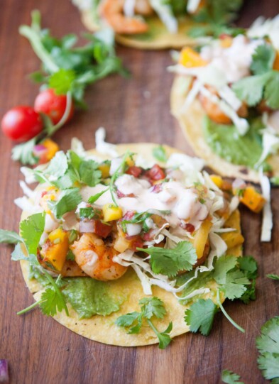 Three shrimp tacos topped with mango salsa and cilantro on top of wood board.