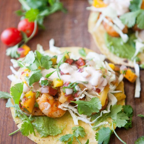 Three shrimp tacos topped with mango salsa and cilantro on top of wood board.