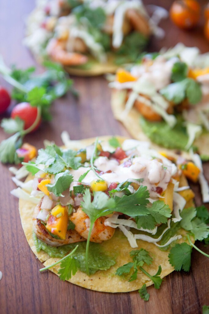 Shrimp taco topped with mango salsa and cilantro on top of wooden cutting board.