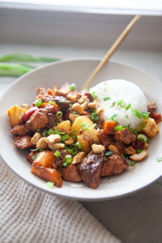 Pineapple chicken stir fry and rice in white bowl with gold spoon.