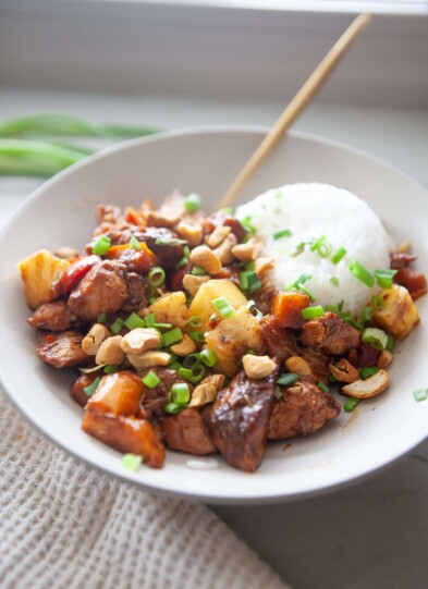Pineapple chicken stir fry and rice in white bowl with gold spoon.