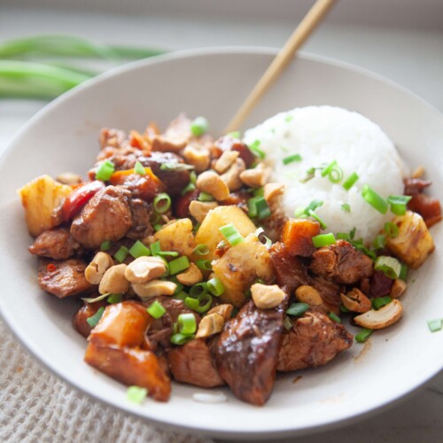 Pineapple chicken stir fry and rice in white bowl with gold spoon.
