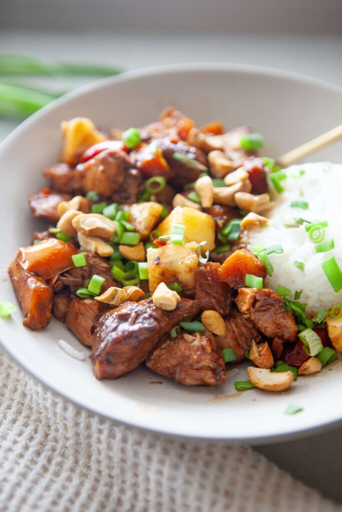 Pineapple chicken stir fry in white bowl with rice and garnished with green onions.