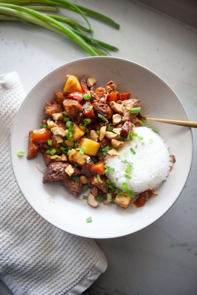 Pineapple chicken stir fry paired with rice in white bowl with gold spoon.