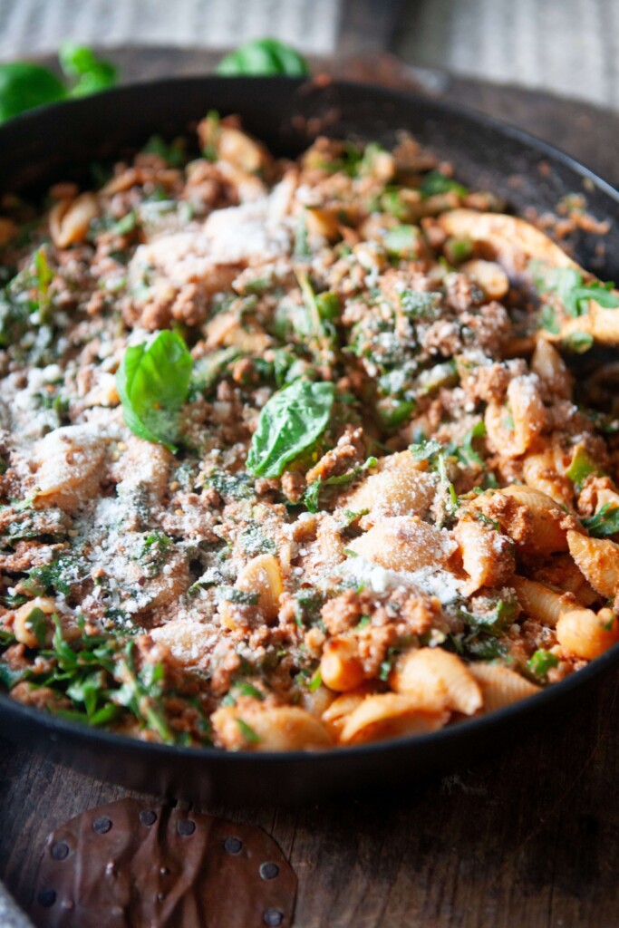 Ground beef and veggie shell pasta recipe in black dish garnished with fresh basil.