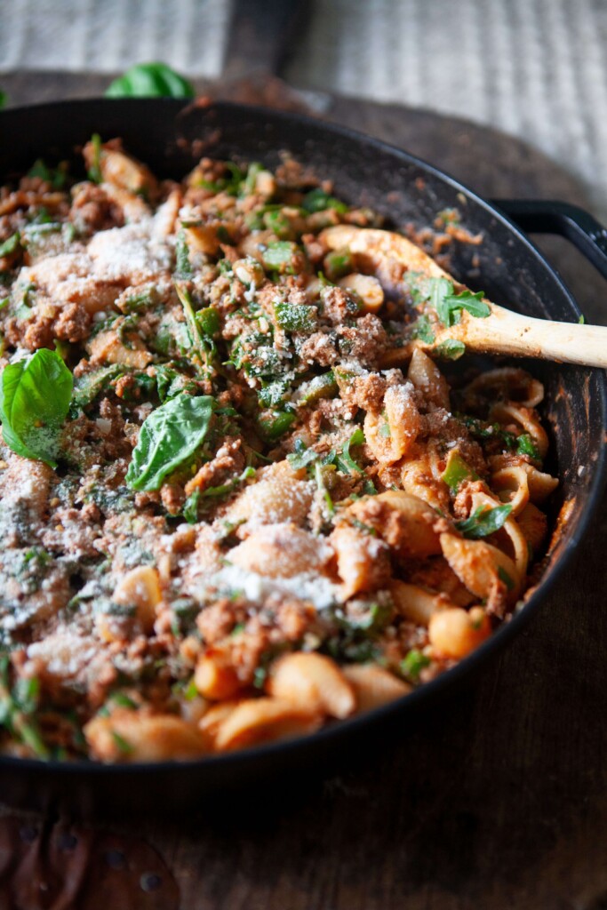 Upclose of beef and veggie shell pasta in cast iron skillet with wood spoon.