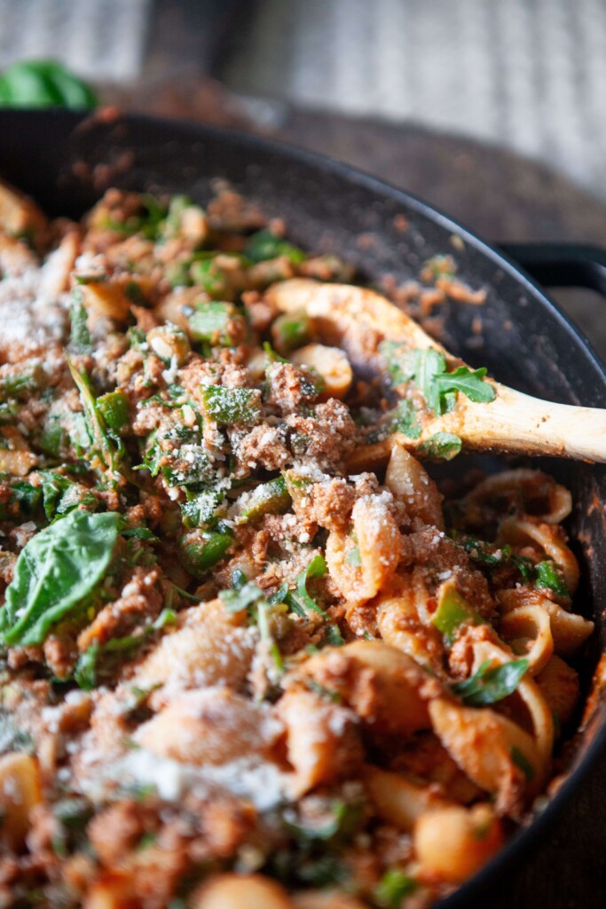 Upclose of beef and shell pasta recipe in large skillet with wood spoon.