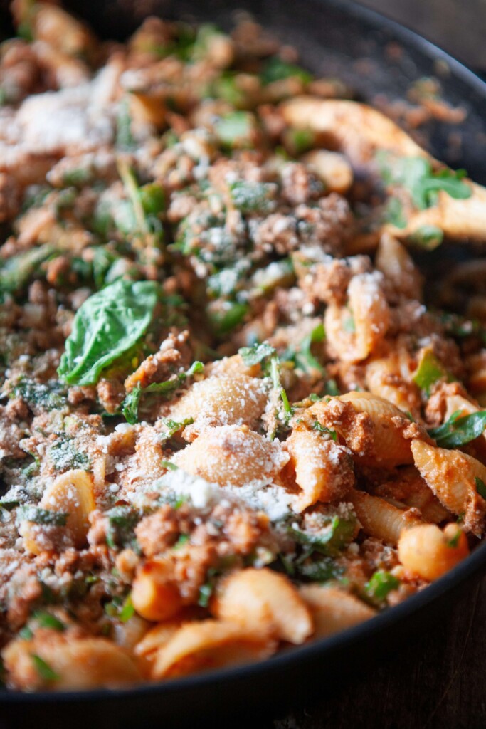 Shell pasta in large skillet with wood spoon to the side.
