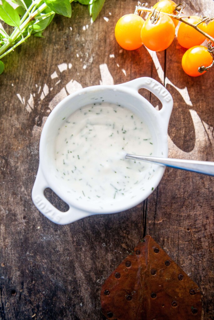 Buttermilk chive dip mixed together in small white bowl with spoon on wood countertop.
