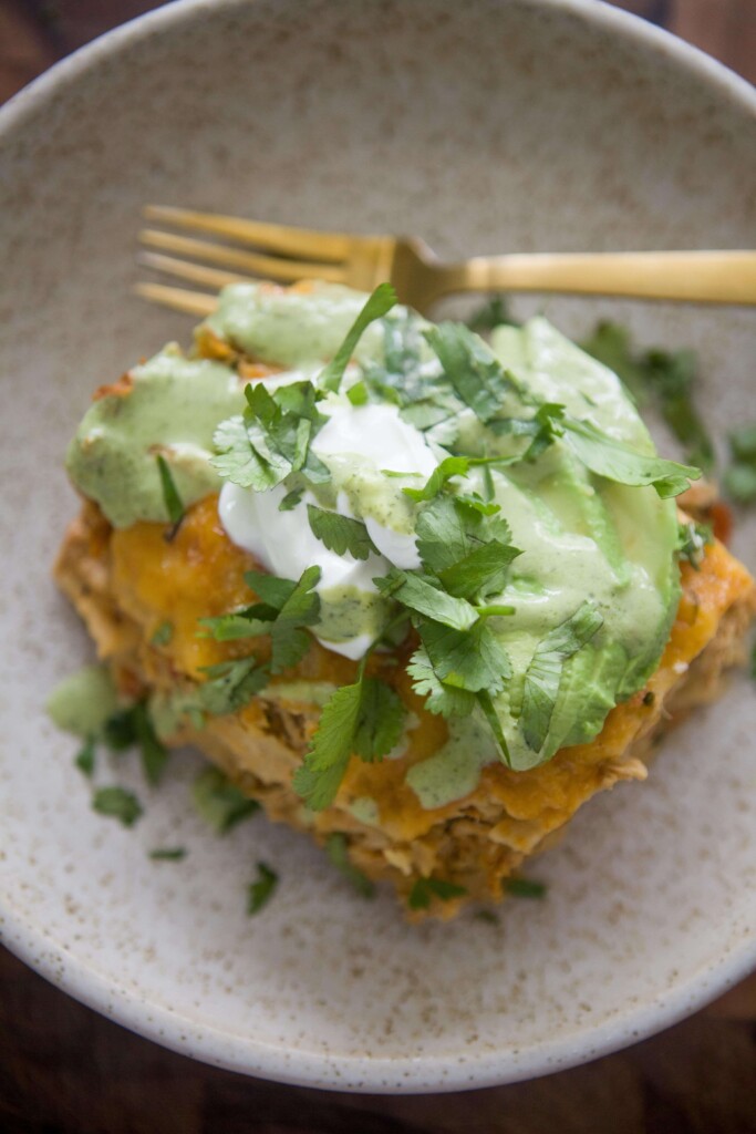 Chicken enchilada casserole topped with lettuce, sour cream and avocado ranch on plate with gold fork.