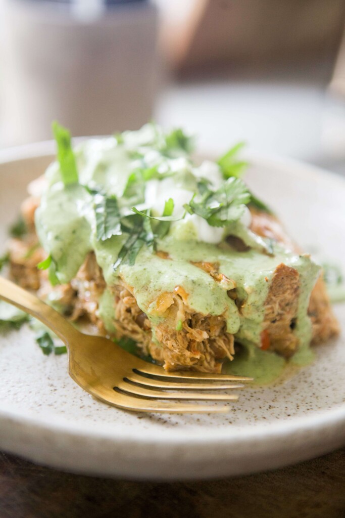 Inside of instant pot chicken enchilada casserole on plate with gold fork topped with lettuce, sour cream and cilantro ranch.