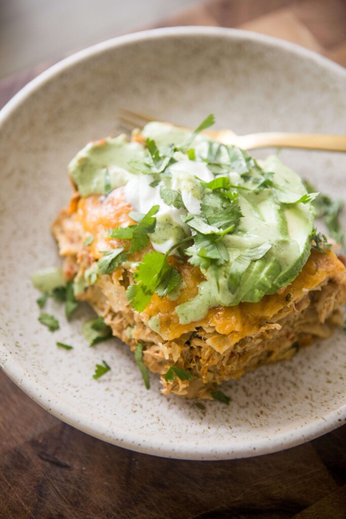Chicken enchilada casserole on white plate with gold fork.