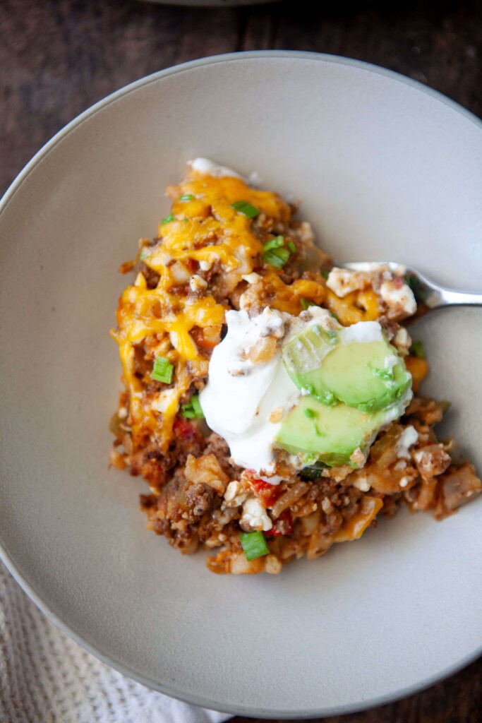 Serving of skillet mexican potatoes on plate topped with sour cream and avocado with fork.