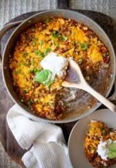 Skillet mexican potatoes in large skillet topped with sour cream and avocado with wood spoon and plate beside skillet with small serving.