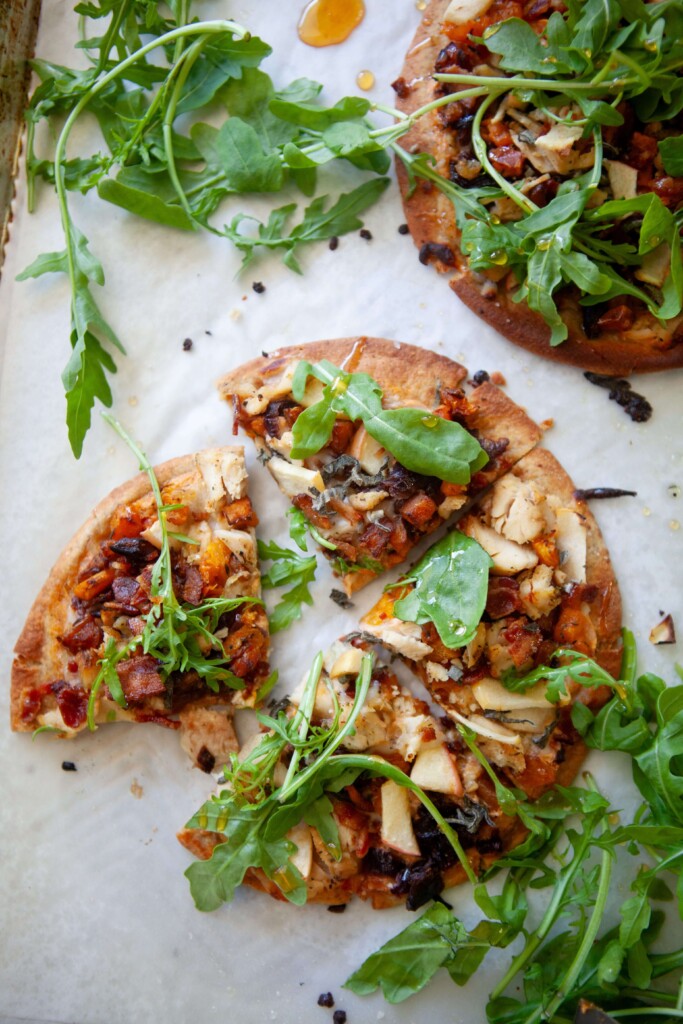 Two butternut squash, bacon and caramelized onion flatbreads on baking sheet with one cut into 4 triangles.