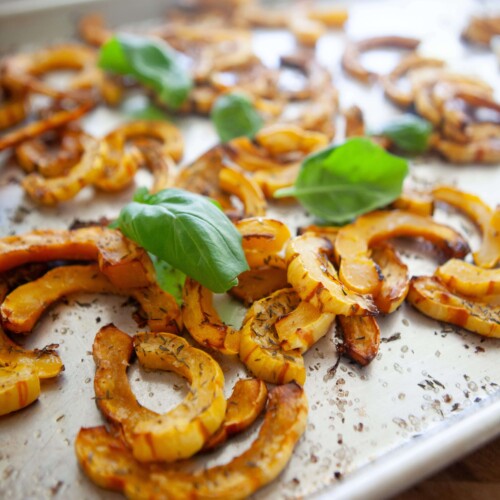 Delicata squash baked on baking sheet garnished with fresh basil.