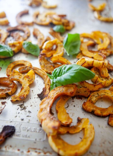 Baked delicata squash on baking tray with fresh basil.