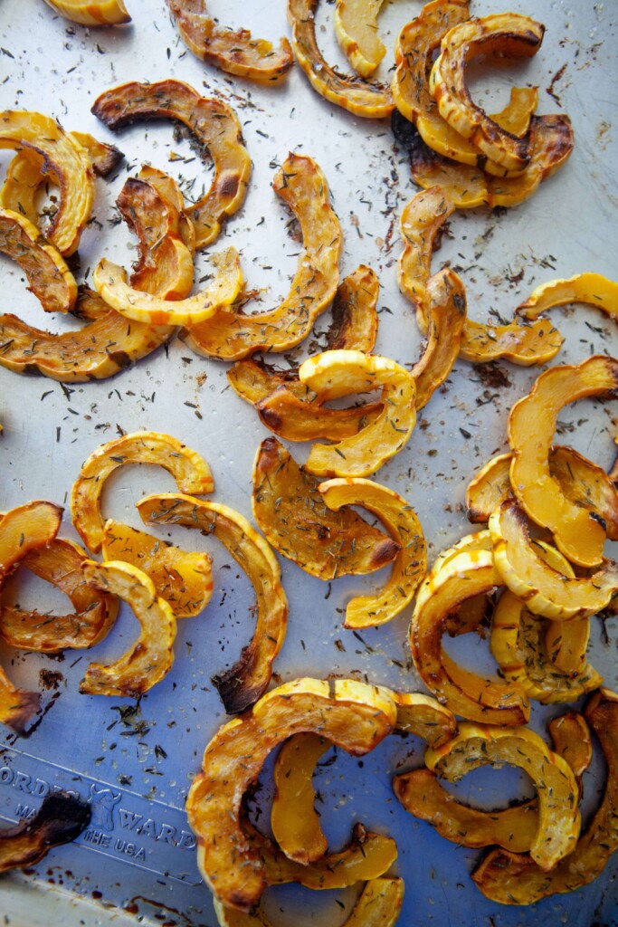 Roasted delicata squash fresh out of the oven on a sheet pan, seasoned with salt and dried herbs, with tender centers and browned, caramelized edges.