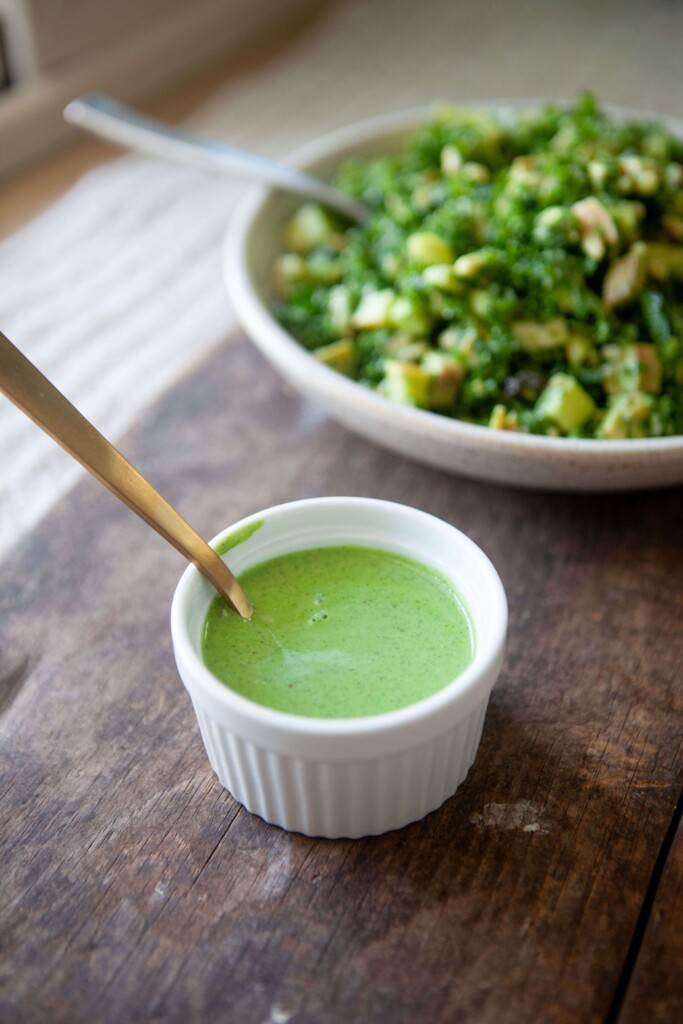 Lemon balsamic cilantro dressing in white ramekin with gold spoon in it.