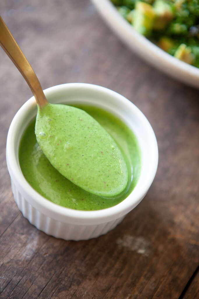 Lemon balsamic cilantro dressing on gold spoon over white ramekin.