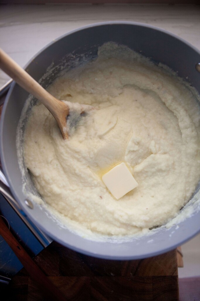 Mashed potatoes and cauliflower in mixing bowl with butter and wooden spoon.