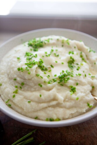 Mashed potatoes and cauliflower garnished with fresh chives in serving bowl.