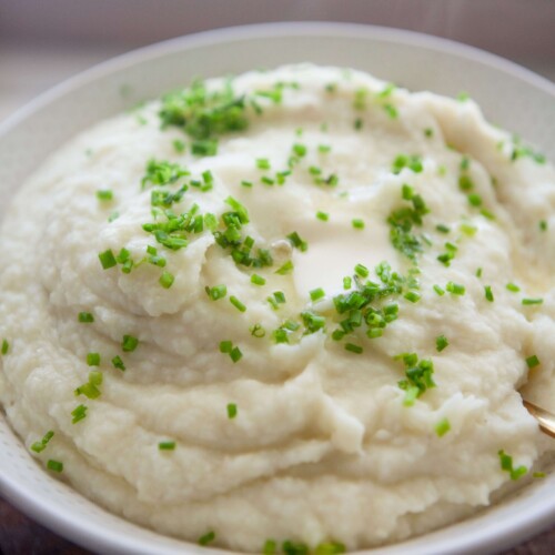 Mashed potatoes and cauliflower garnished with fresh chives in serving bowl.
