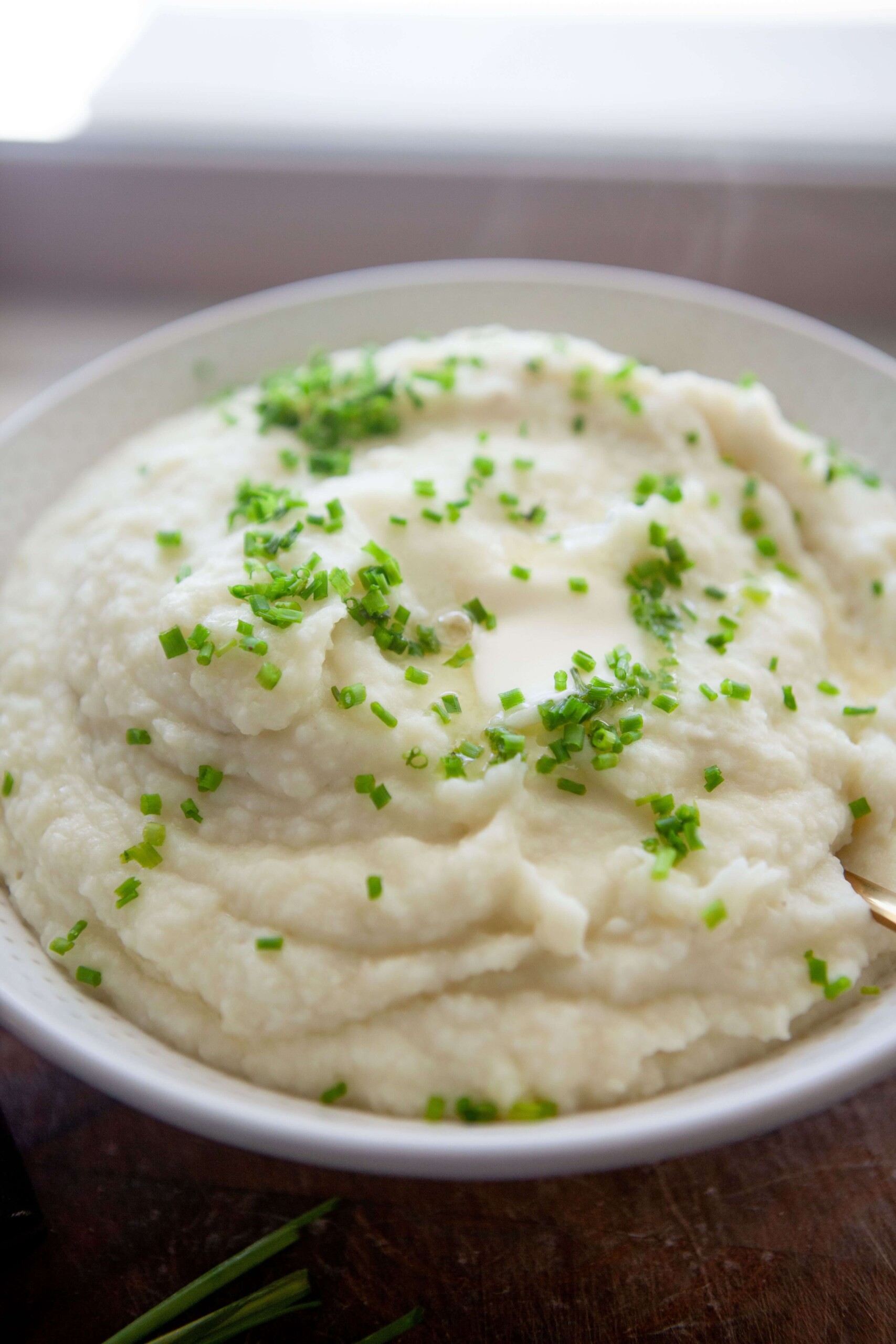 Mashed potatoes and cauliflower garnished with fresh chives in serving bowl.