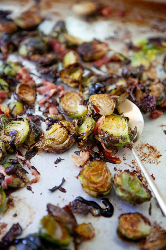 Spoon scooping up roasted brussels sprouts on baking pan.