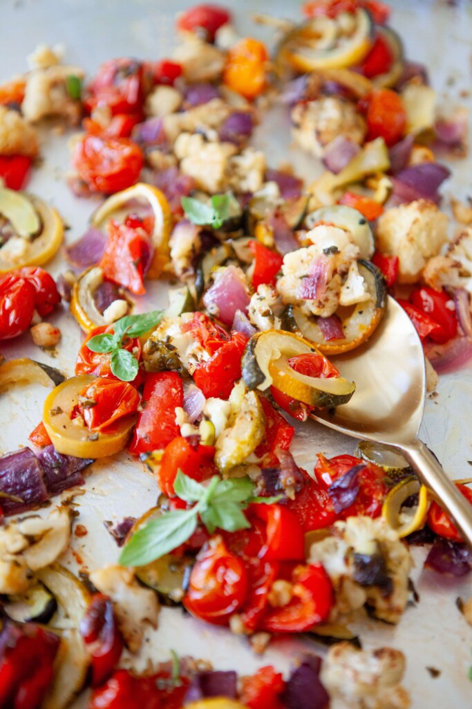 Gold spoon digging into basil roasted veggies on large sheet pan.