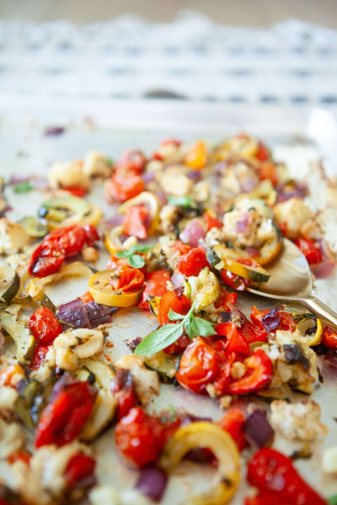 Spoon scooping basil roasted veggies off large sheet pan.