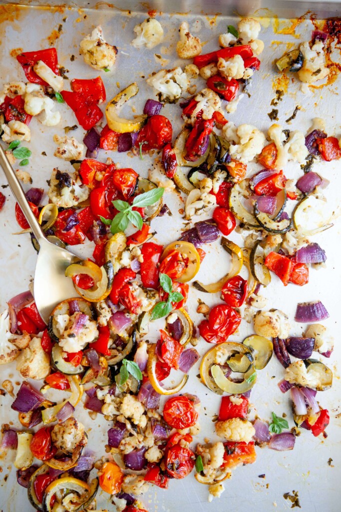 Spoon scooping up basil roasted veggies off large sheet pan.