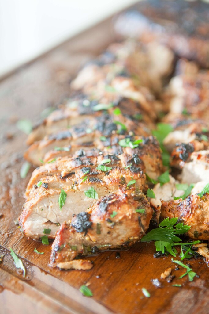 Balsamic pork tenderloin cut on wood board and sprinkled with fresh herbs.