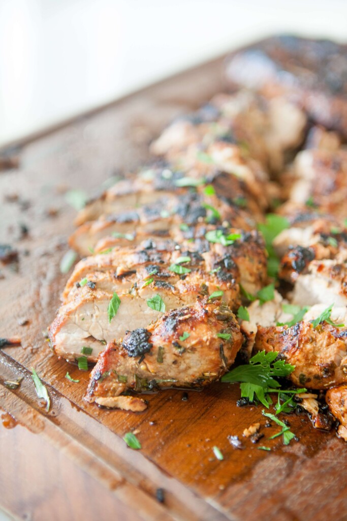 Balsamic and herb pork tenderloin grilled and cut on wood cutting board.
