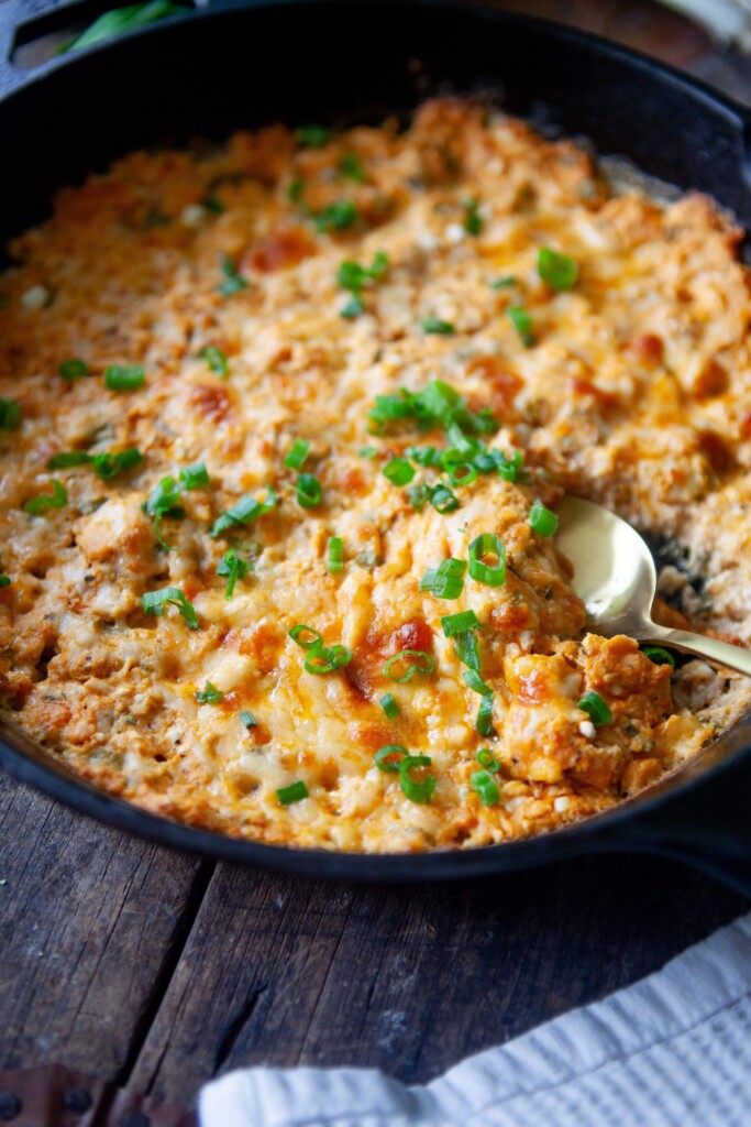 Spoon digging into healthy buffalo chicken dip in cast iron skillet.