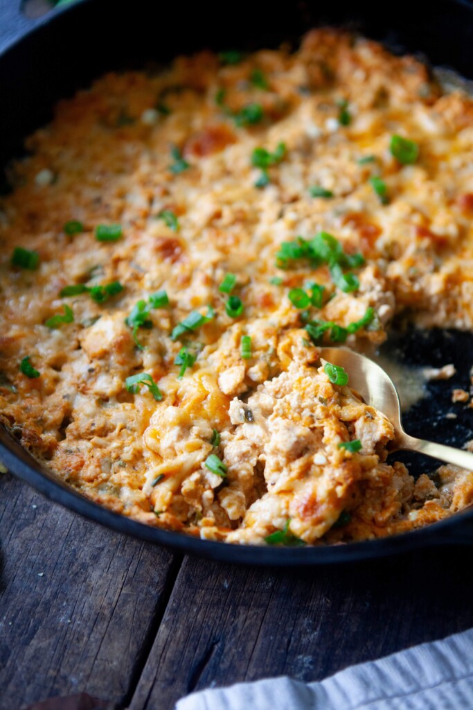 Spoon digging out some healthy buffalo chicken dip out of cast iron skillet.