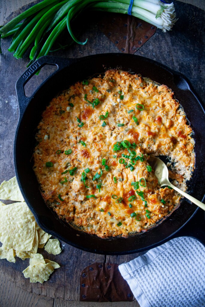 Buffalo chicken dip in a cast iron skillet with spoon and garnished with green onions.