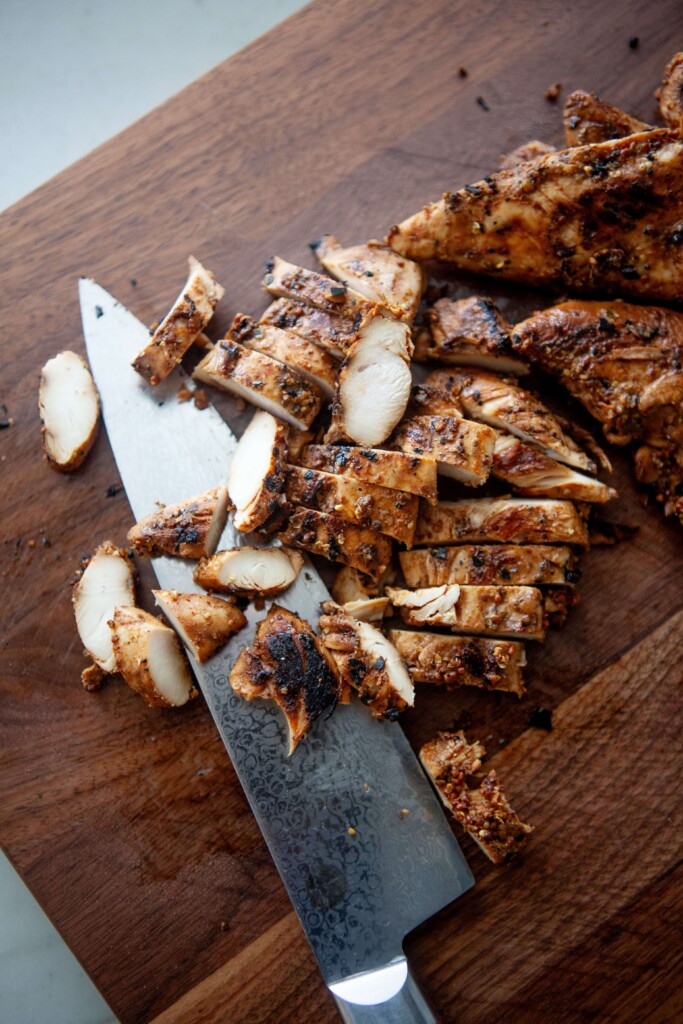 Balsamic, dijon, garlic chicken tenders sliced with knife on wood cutting board.
