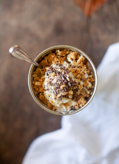 A cup of a frosty protein shake topped with rice crispies, chocolate nibs, whipped cream, protein bars, and more!