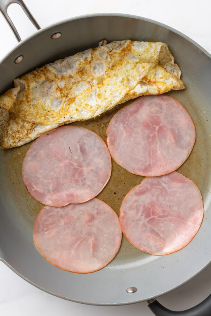 Four pieces of ham cooked in hot pan with egg whites pushed to the side.