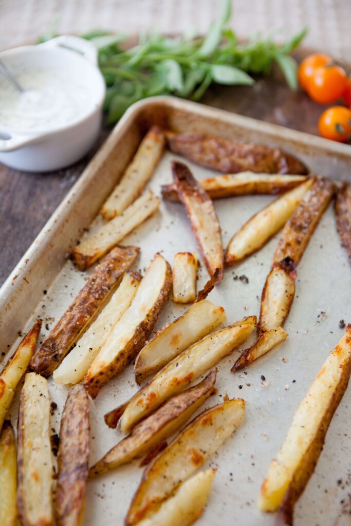 Oven roasted fries boiled and baked on metal baking sheet in the oven.