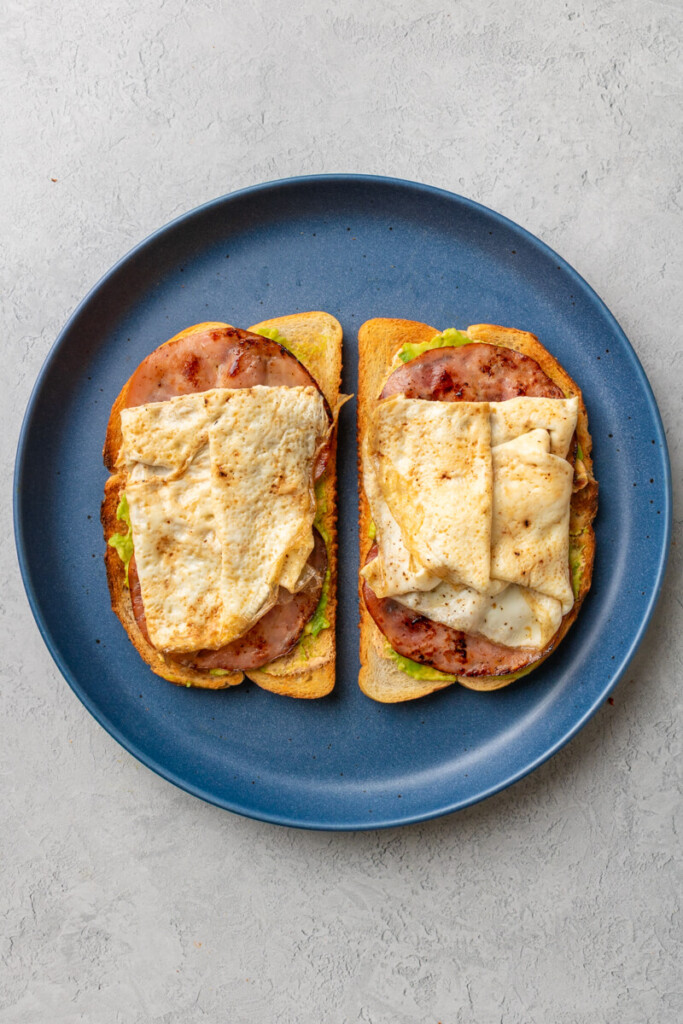 Toast topped with chipotle cream, avocado, ham and egg whites on a blue plate.